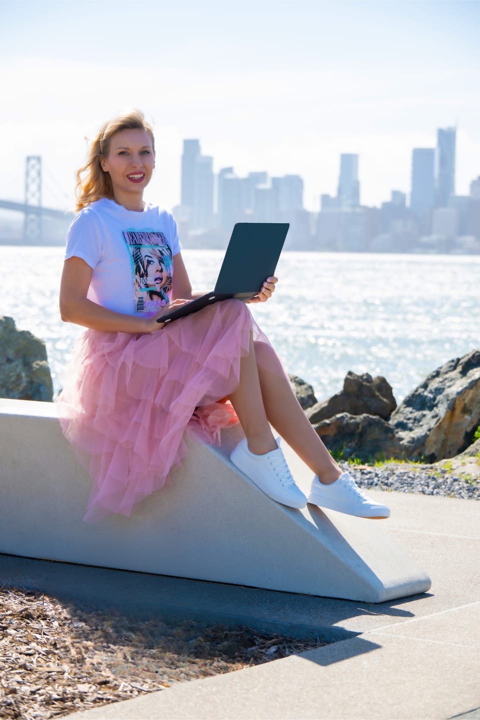 Sylvia Gorajek of America Unlocked smiling with a laptop by the water, San Francisco skyline behind her, on EB-1A self-sponsored visa requirements